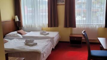 Una habitación de hotel con dos camas, un escritorio, una silla y una ventana con cortinas.