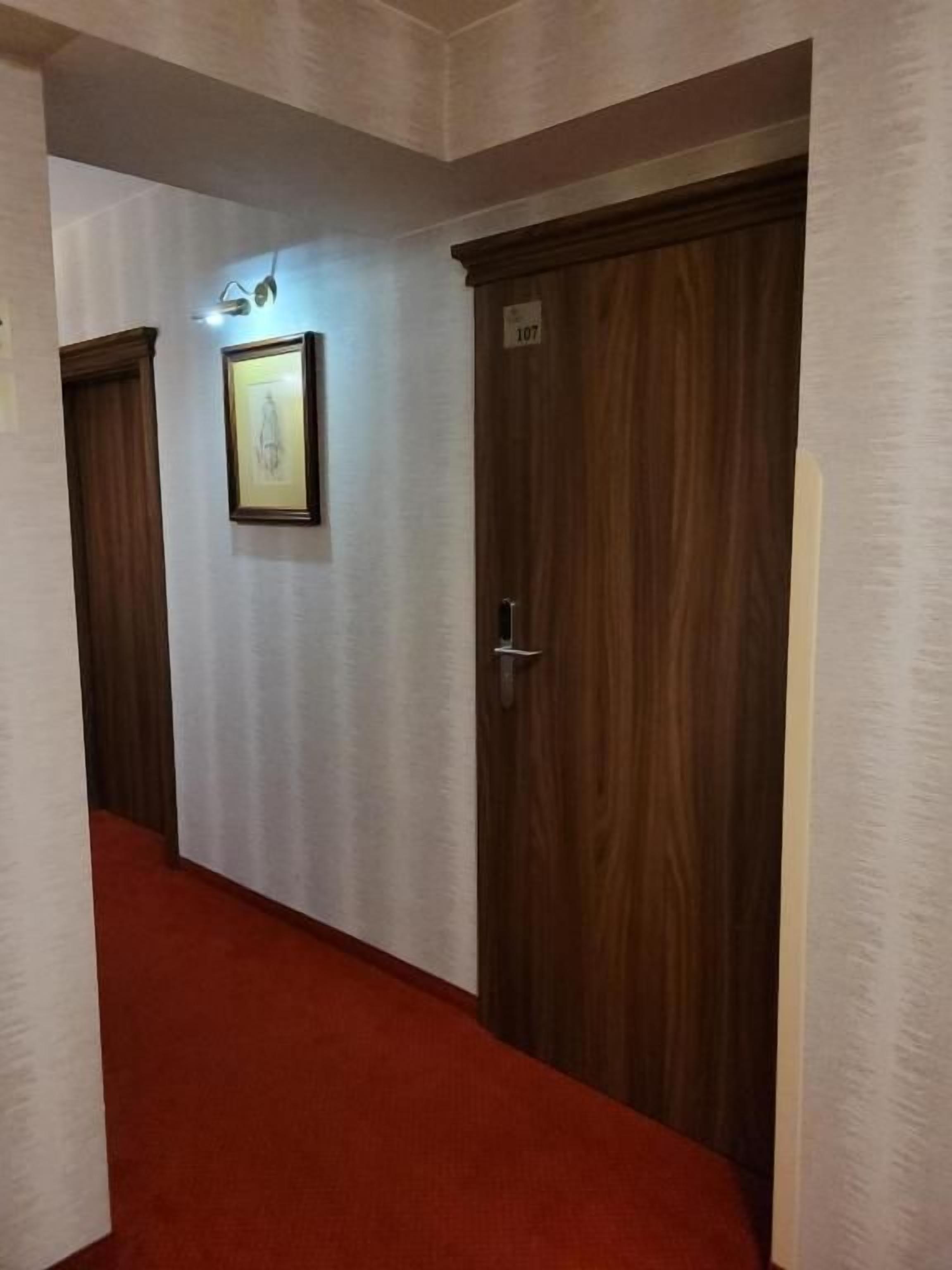 A hallway with a red carpet leading to a door marked with the number 107.