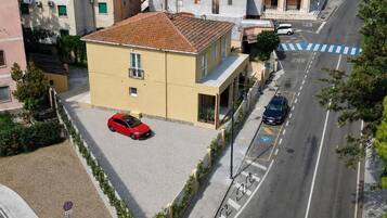 Un bâtiment à deux étages, avec un toit recouvert de tuiles, une voiture garée devant, et une route marquée d’une ligne bleue, avec une voiture blanche.