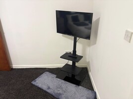 A corner setup with a TV on a stand, a remote control on the stand, and a small table.