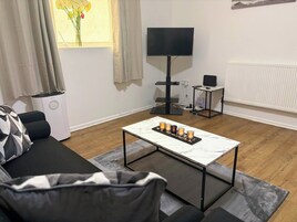 A living room with a sofa, a coffee table with candles, a TV, and a radiator.