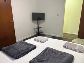 Ein Hotelzimmer mit einem Bett, einem an der Wand befestigten Flachbildfernseher und einer Tür zu einem anderen Raum.