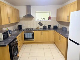 A kitchen with wooden cabinets, a gas stove, a microwave, a washing machine, and a window with a view.