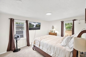 A bedroom with a bed, a standing fan, a TV, and a window with curtains. - Cozy 3BR Home Base | Coffee Bar | Massive Backyard (Abilene)
