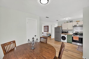A dining area with a wooden table and chairs, a kitchen with appliances, and a living room with a sofa and a painting. - Cozy 3BR Home Base | Coffee Bar | Massive Backyard (Abilene)