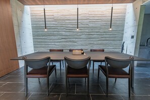 A modern dining area with a long table and four chairs, a wooden accent wall, and pendant lighting. - CASA MIYAKO II PREMIUM (Miyakojima)