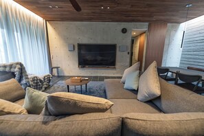 A modern living room with a large flat-screen TV mounted on a wall, a sofa set, a coffee table, and a small side table. - CASA MIYAKO II PREMIUM (Miyakojima)
