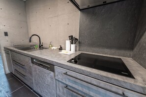 A modern kitchen with a built-in dishwasher, a black stovetop, and a marble countertop. - CASA MIYAKO II PREMIUM (Miyakojima)