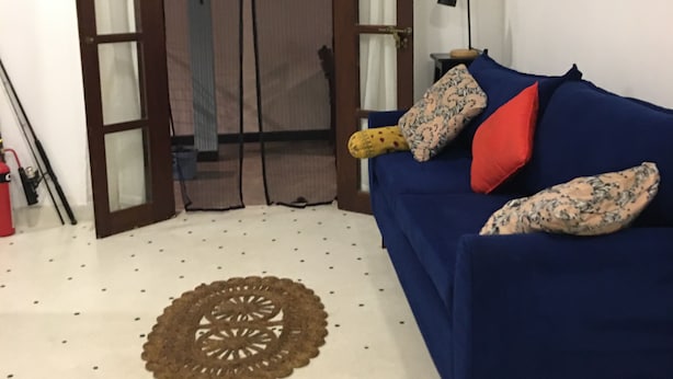 Une pièce avec un canapé bleu, un tapis à motifs, une porte avec des panneaux de verre et une lampe fixée au mur.