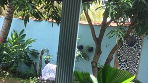 Un espace jardin agrémenté de diverses plantes en pot, d’une colonne en métal et d’un mur recouvert de carreaux.