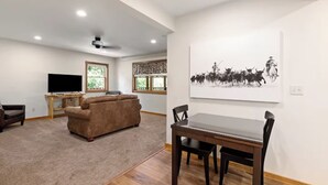 A living room with a sofa, TV, and a dining area with a table and chairs. - Margaret Bridge Suite at Rim Rock Lodge (Spearfish)