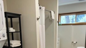 A bathroom with a shower, toilet, and a shelf with towels. - Margaret Bridge Suite at Rim Rock Lodge (Spearfish)