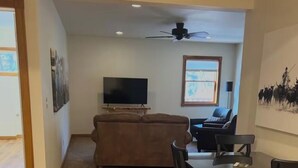 A living room with a sofa, a television, a ceiling fan, and a dining area with a table and chairs. - Margaret Bridge Suite at Rim Rock Lodge (Spearfish)