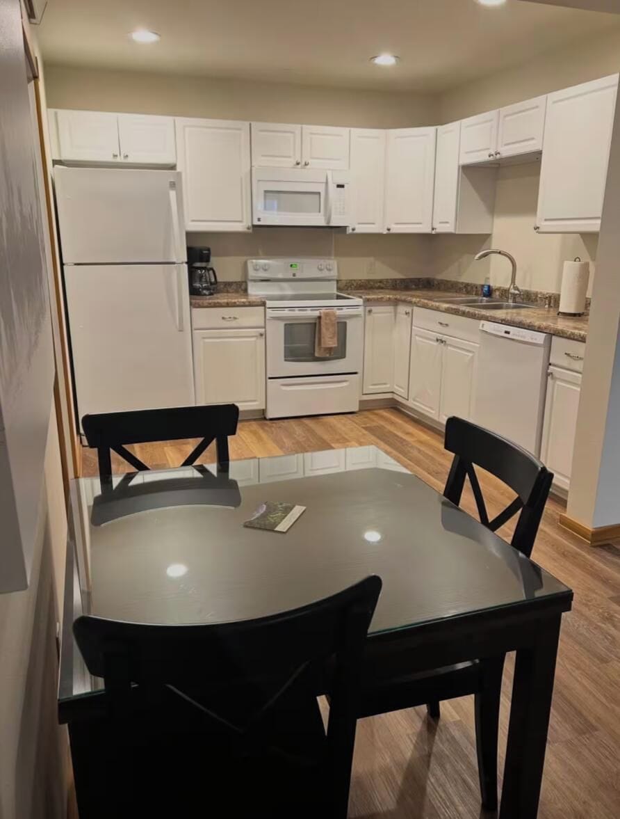 A compact kitchen with white cabinets, a refrigerator, microwave, stove, and a dining table with chairs.