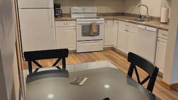 A compact kitchen with white cabinets, a refrigerator, microwave, stove, and a dining table with chairs.