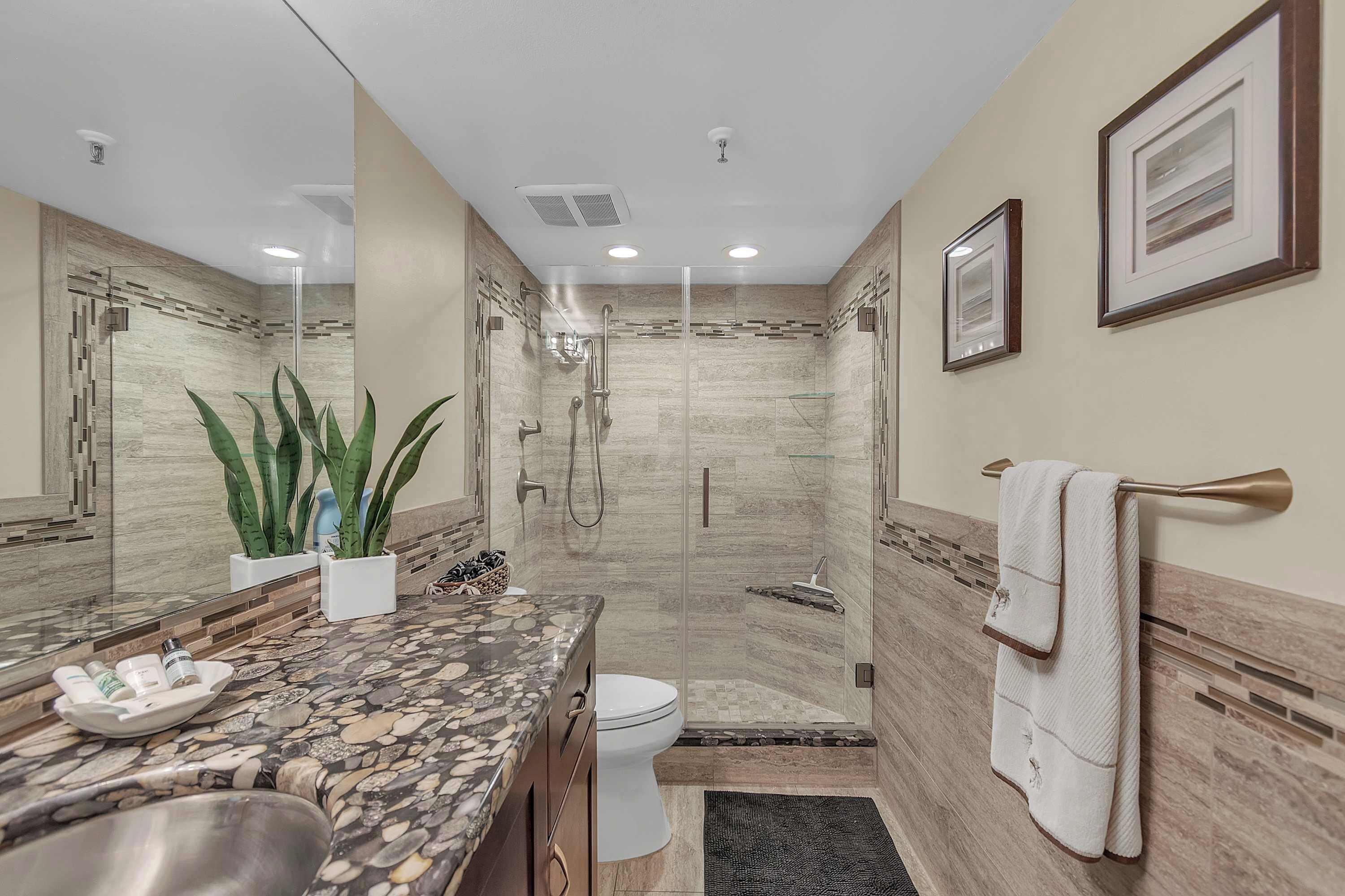 Un baño moderno con ducha envuelta en cristal, tocador de mármol y un espejo grande.