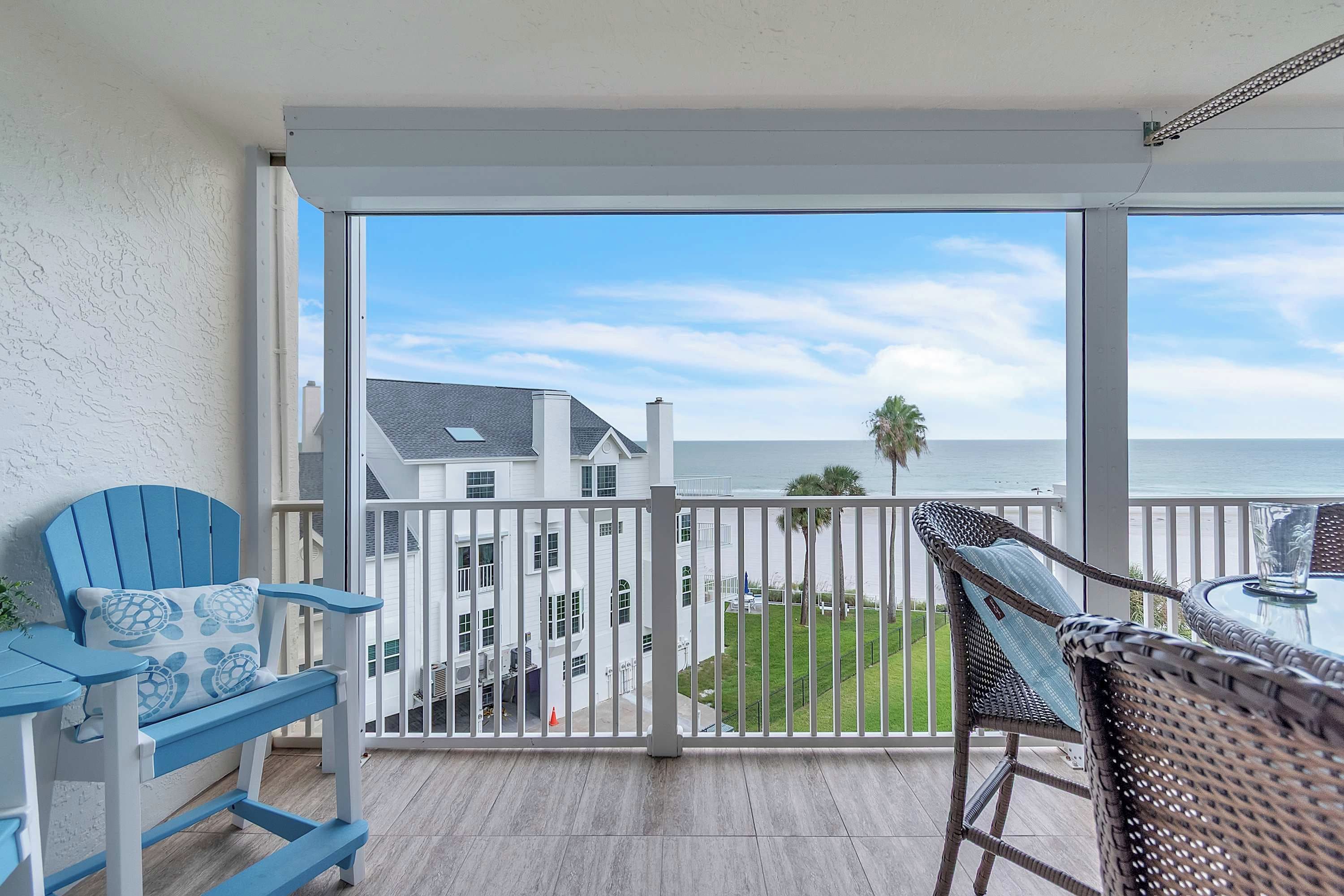 A balcony with a view of the ocean, a wicker chair, a blue bench, and a table.