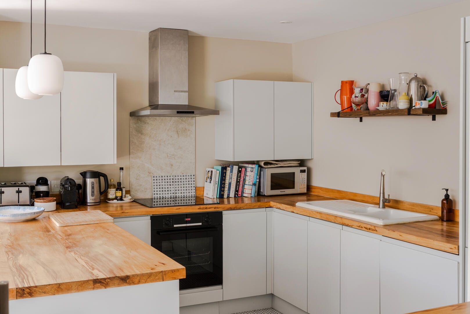 Una cocina moderna con armarios blancos, encimera de madera, horno integrado, microondas y campana extractora de acero inoxidable.