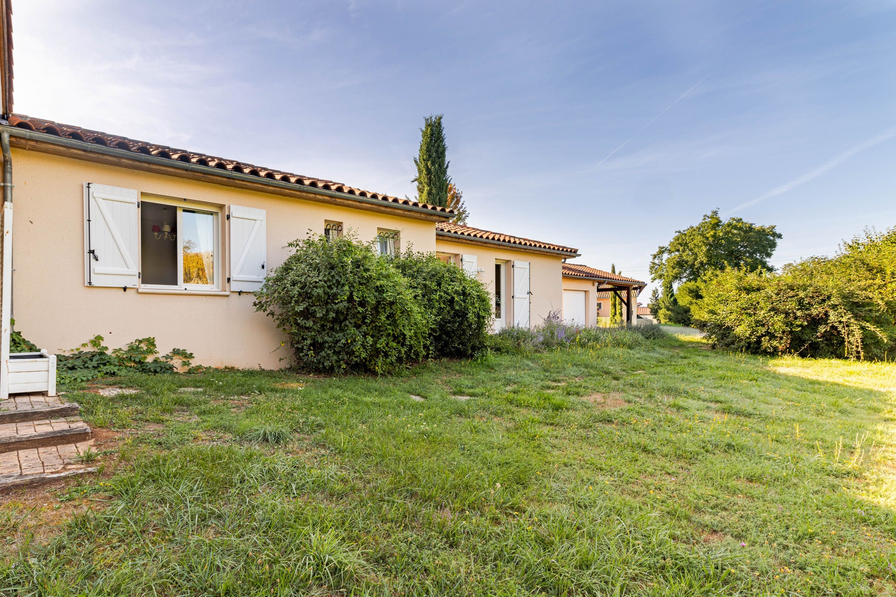 Une maison à deux étages, avec un toit recouvert de tuiles, un jardin à l’avant et un chemin menant à l’entrée.