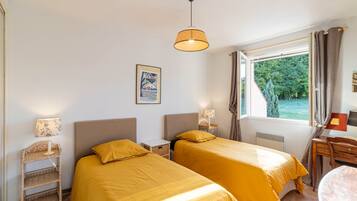 Une chambre avec deux lits, une fenêtre avec des rideaux, une lampe et un tableau encadré au mur.