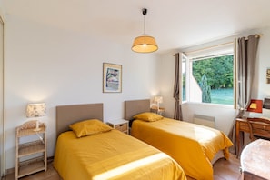 A room with two beds, a window with curtains, a lamp, and a framed picture on the wall. - Lou Poutou du Levant - maison avec jardin privé (Gramat)