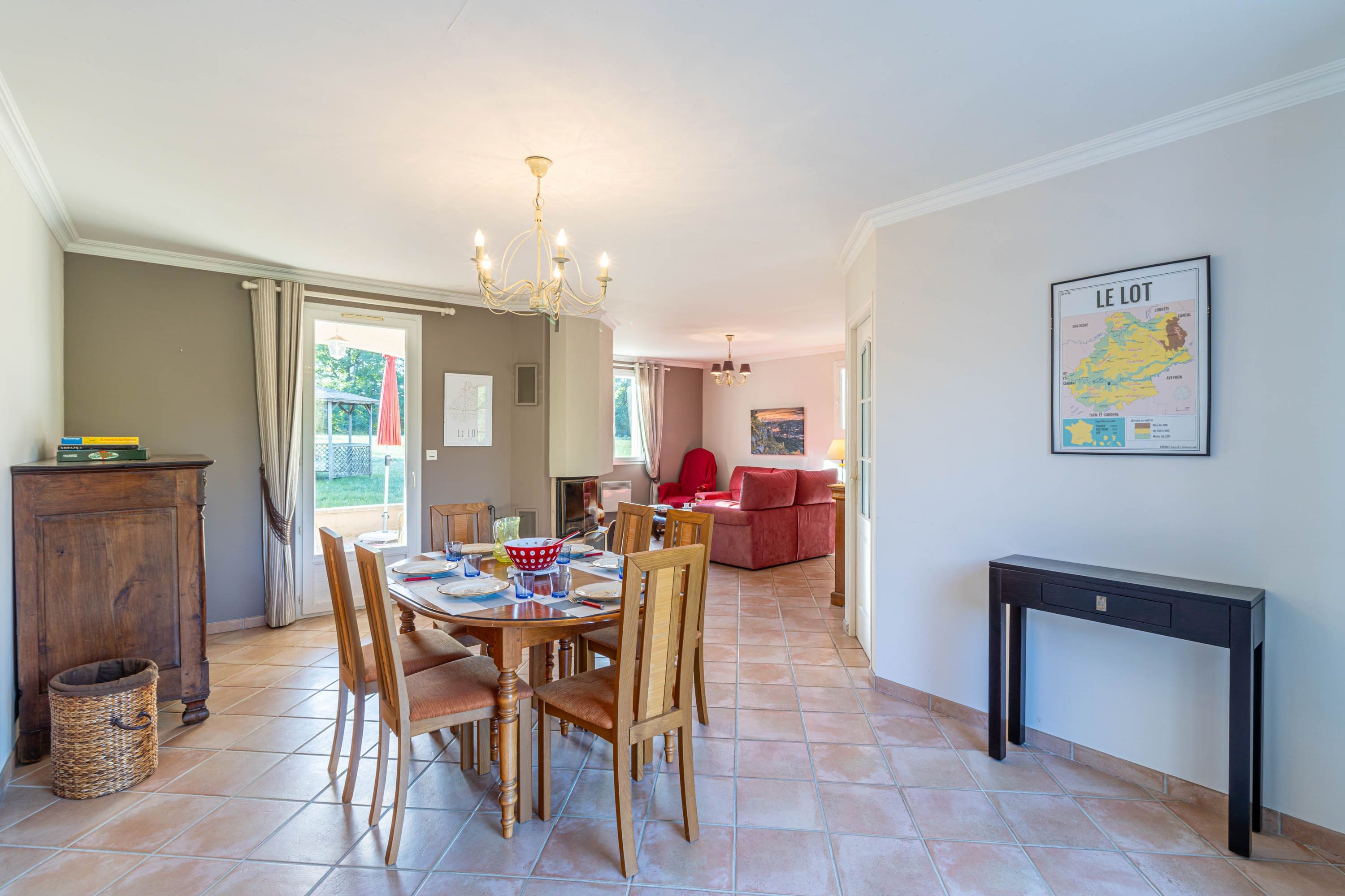 Een eetgedeelte met een ronde tafel, stoelen en een kroonluchter. Er hangt een kaart aan de muur en er staat een bank op de achtergrond.
