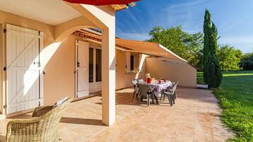 Un patio couvert avec une table dressée pour le repas, une chaise en osier et un parasol rouge.