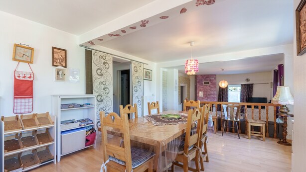Un espace repas avec une table et des chaises en bois, un coin cuisine avec des placards et un évier, et un couloir agrémenté d’un plafond décoratif.
