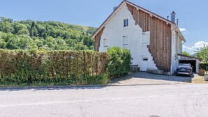 Une maison à deux étages avec un garage, une voiture garée à l’intérieur et une haie devant.