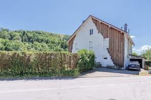 Ein zweistöckiges Haus mit Garage, ein Auto steht darin geparkt, und ein Hecken befindet sich davor.