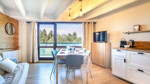 Ein modernes Zimmer mit Esstisch, Stühlen, einer Sitzecke, einem Fernseher und einer Küchenzeile.