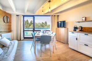 Ein modernes Zimmer mit Esstisch, Stühlen, einer Sitzecke, einem Fernseher und einer Küchenzeile.