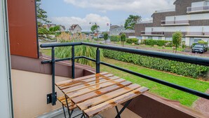 Een balkon met een houten tafel en een metalen hekwerk, met uitzicht op een woonwijk met huizen en een weg.