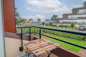 Ein Balkon mit Holztisch und Metallgeländer, der auf ein Wohngebiet mit Häusern und einer Straße blickt.