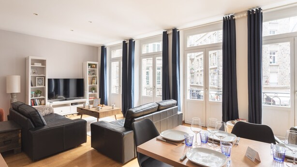 A modern living room with a sofa, a TV, and a dining area with a table set for two. - La Croix du Fief - Dans Intra Muros (Saint-Malo)