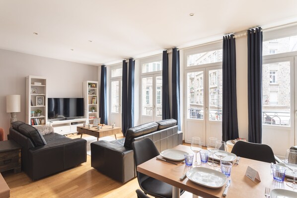 Un salon moderne avec un canapé, un téléviseur et un coin repas avec une table mise pour deux personnes.