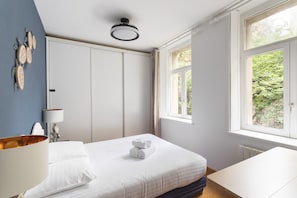 Une chambre à coucher comprenant un lit, une table de chevet, une lampe, une fenêtre et un mur décoré.