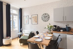 Une cuisine moderne avec une table à manger pour quatre personnes, une machine à café et une horloge au mur.