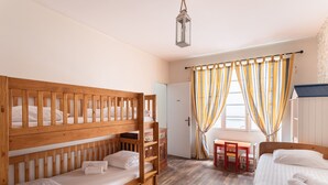 Quarto com beliches, uma mesa de madeira e uma janela com cortinas.
