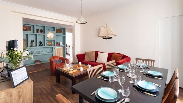 Uma sala de jantar com mesa posta para quatro pessoas, um sofá vermelho e parede azul decorada.