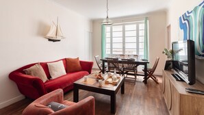 Uma sala de estar com sofá vermelho, mesa de centro e área de jantar com cadeiras e mesa de madeira.
