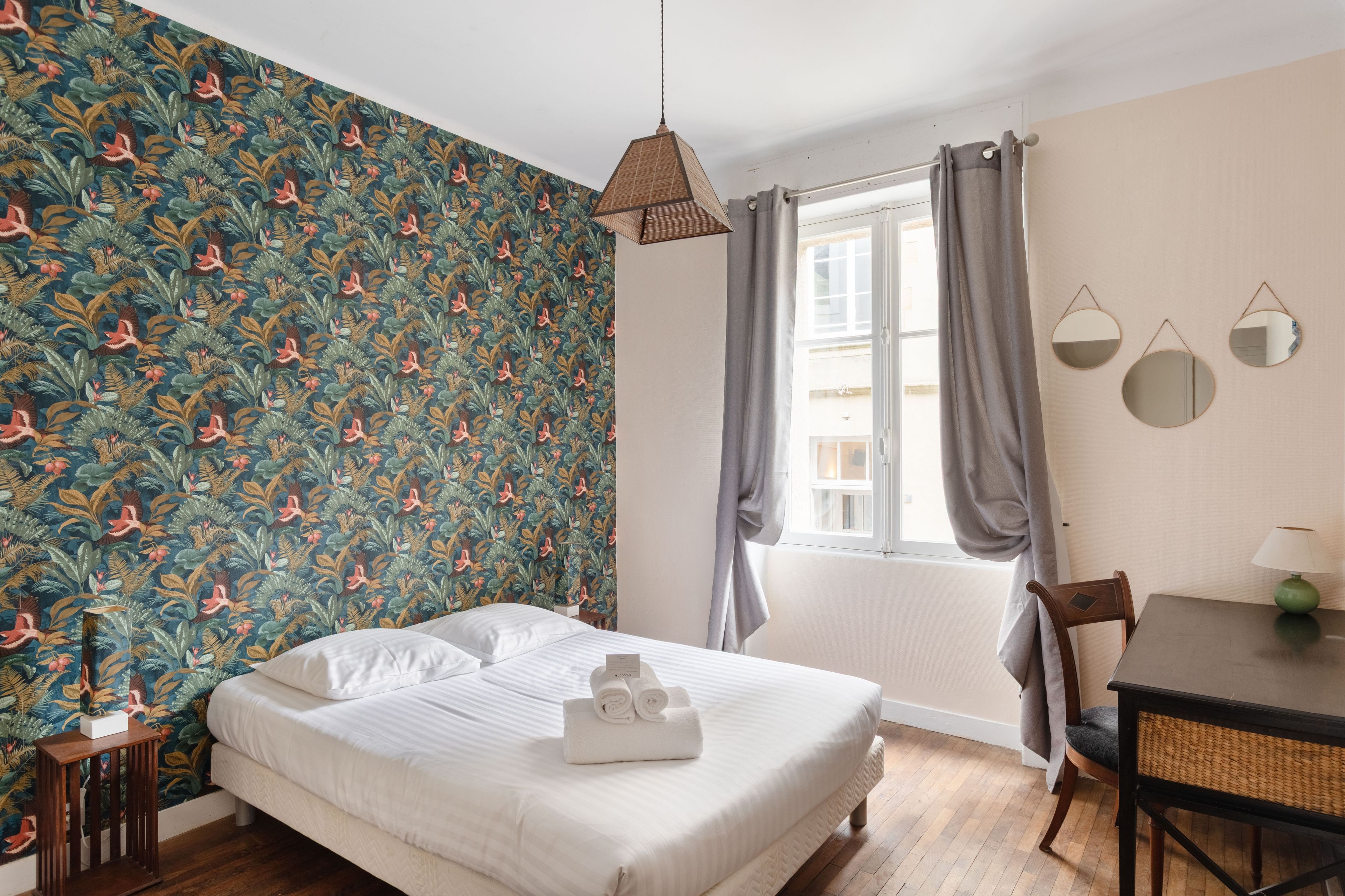 Habitación de hotel con cama, mesa, silla y ventana con cortinas.