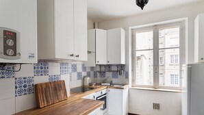 Cozinha compacta com armários brancos, máquina de lavar Bosch e janela com vista para prédios.