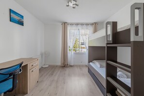A compact hotel room with a bunk bed, a desk with a chair, a standing fan, and a window with curtains. - ArcachonAir plein centre dArcachon à 2 pas de la plage (Arcachon)