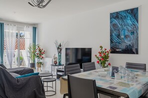A modern dining area with a table set for four, a flat-screen TV, and decorative plants. - ArcachonAir plein centre dArcachon à 2 pas de la plage (Arcachon)