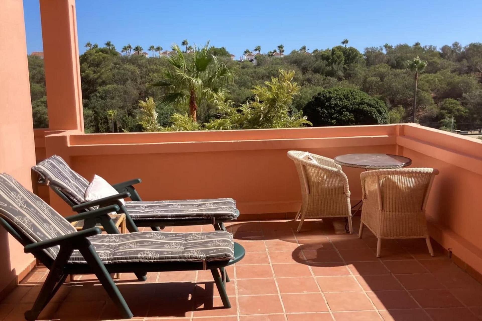 Une terrasse avec des fauteuils de jardin, une petite table et une vue sur une colline boisée.