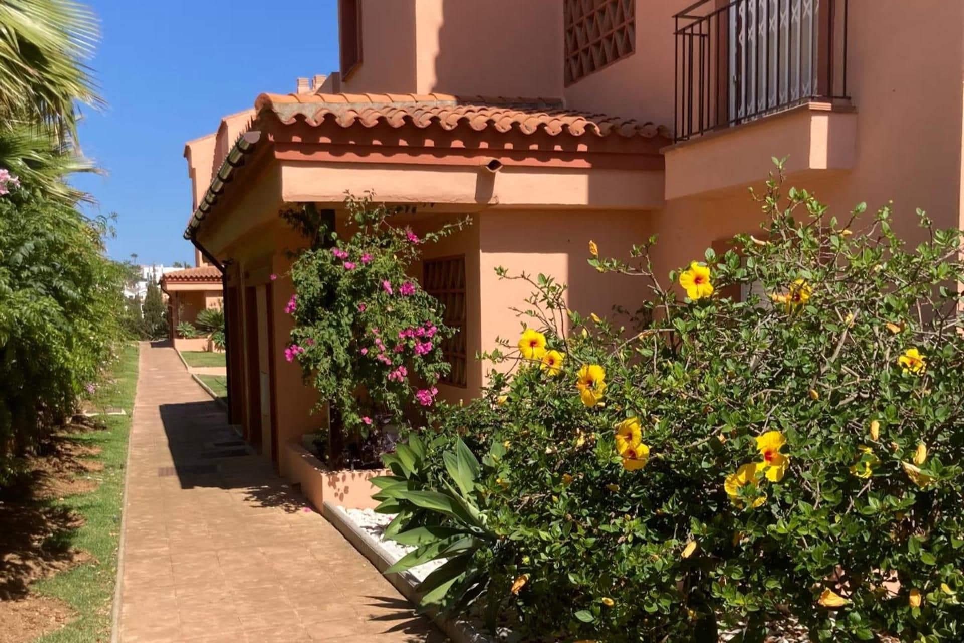 A pathway leading to a building with a tiled roof and a balcony with a metal railing.