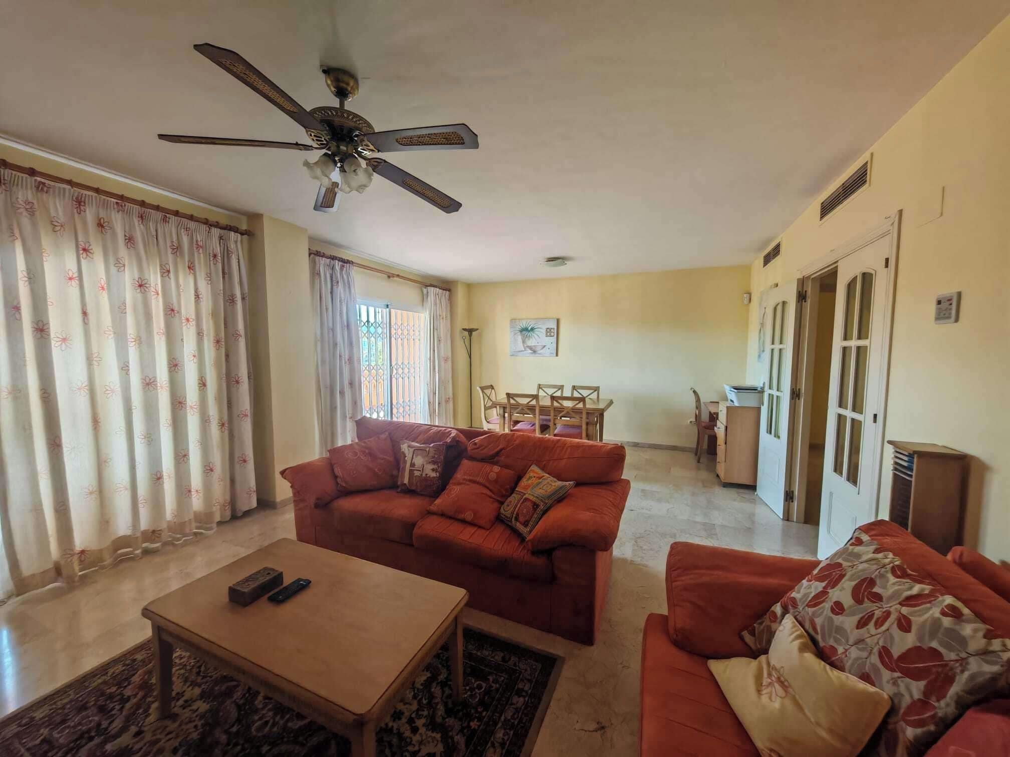 Un salon comprenant un canapé, une table basse, un ventilateur de plafond et un coin repas avec une table et des chaises.