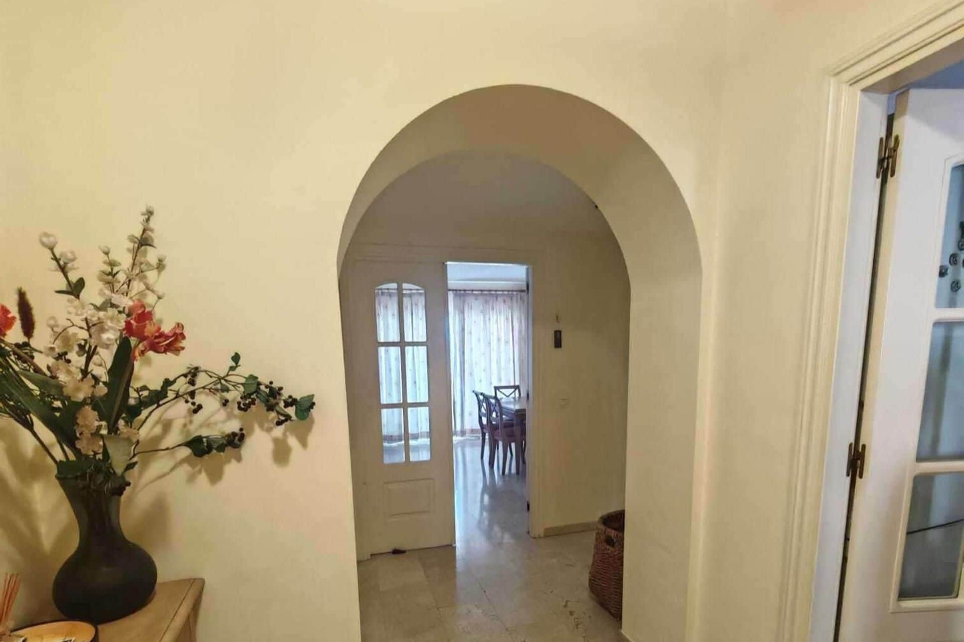 Un couloir intérieur avec une porte en arc donnant accès à une salle à manger.