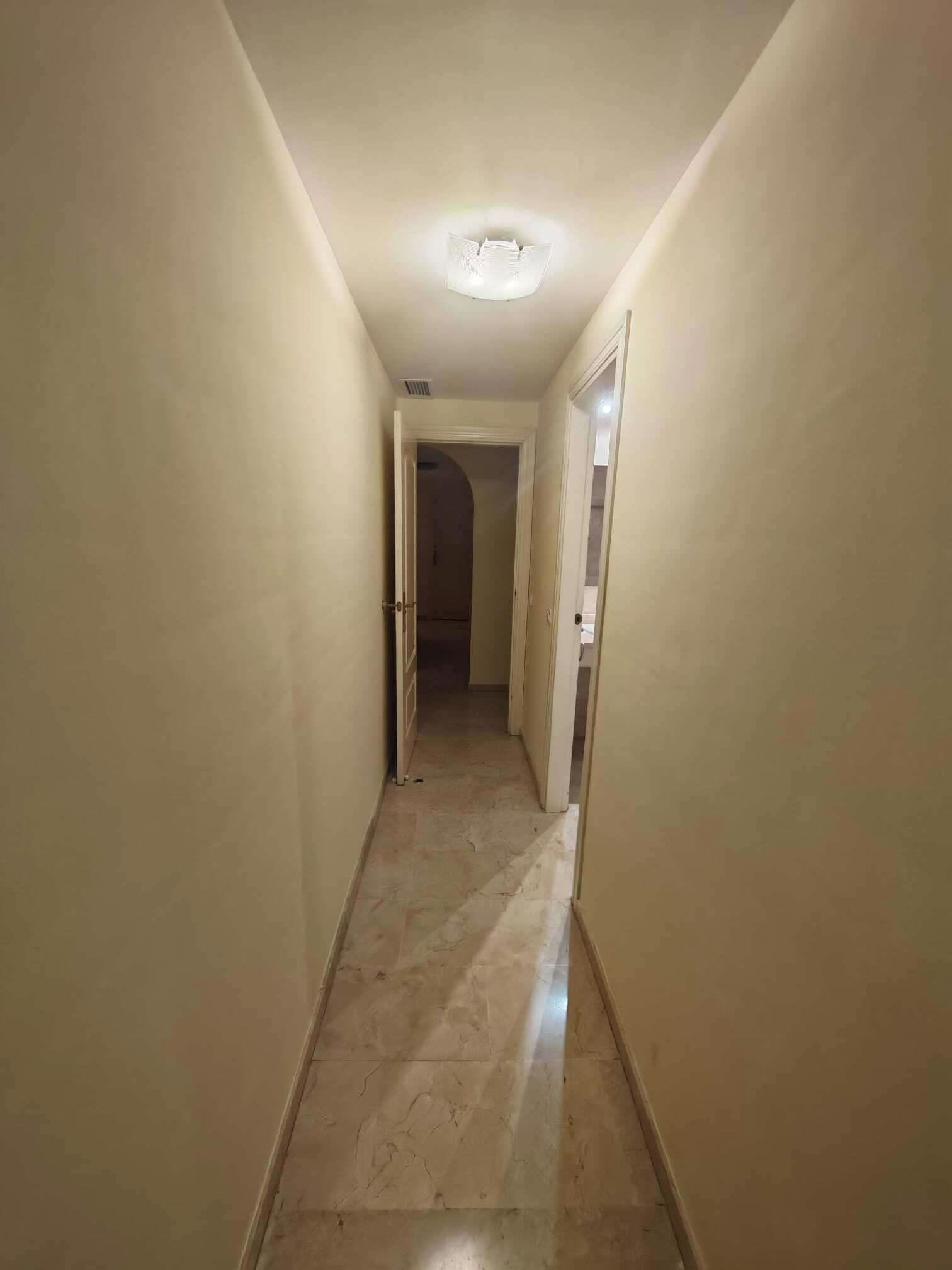A narrow hallway with a ceiling light, leading to a door at the end.